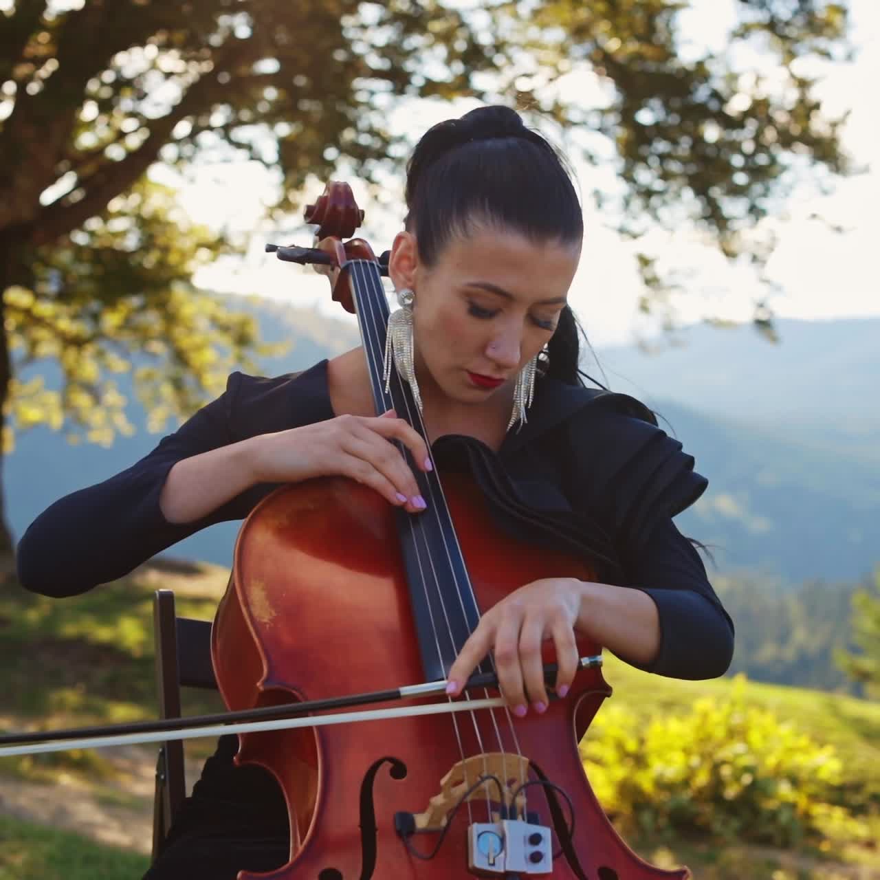 Pretty lady playing cello on nature landscapes. Summer instrumental perfomance woman player