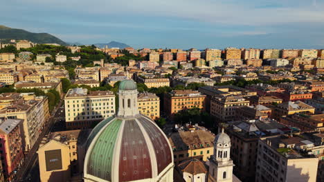 drone orbits above the dome of genoa’s cathedral of san lorenzo during the golden hour, showcasing the city’s colorful buildings, hillside housing, mountains, and sea in the distance
