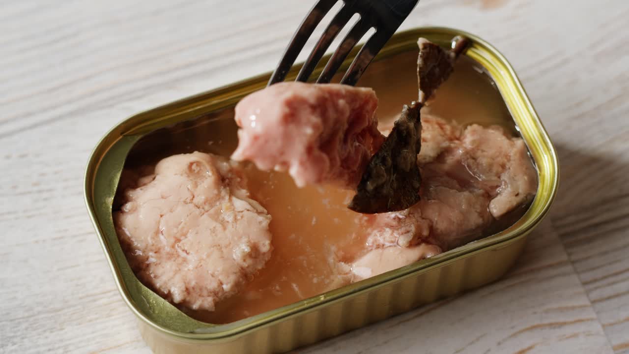 Smoked cod liver in oil in open tin can with fresh greens on wooden table. Seafoods delicacy. High quality 4k footage