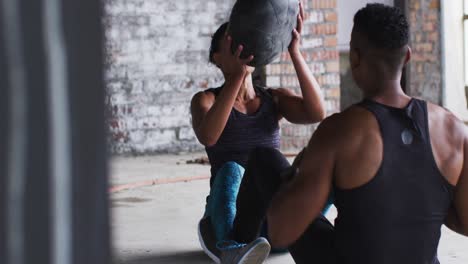 hombre y mujer afroamericanos haciendo ejercicio con una pelota de medicina en un edificio urbano vacío