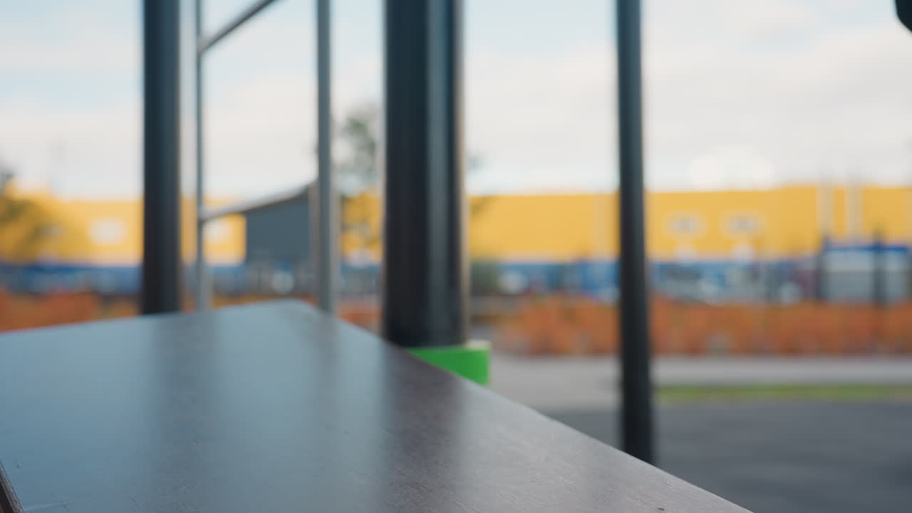 Fitness enthusiast in hooded tracksuit sets sports bag on urban calisthenics bar corner then bends gracefully to tie shoelace on bar before starting dynamic outdoor workout by modern apartment