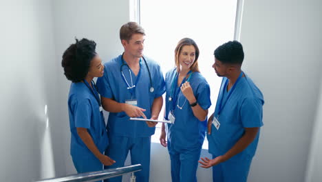 multi cultural medical team wearing scrubs meeting on stairs in hospital discussing patient chart