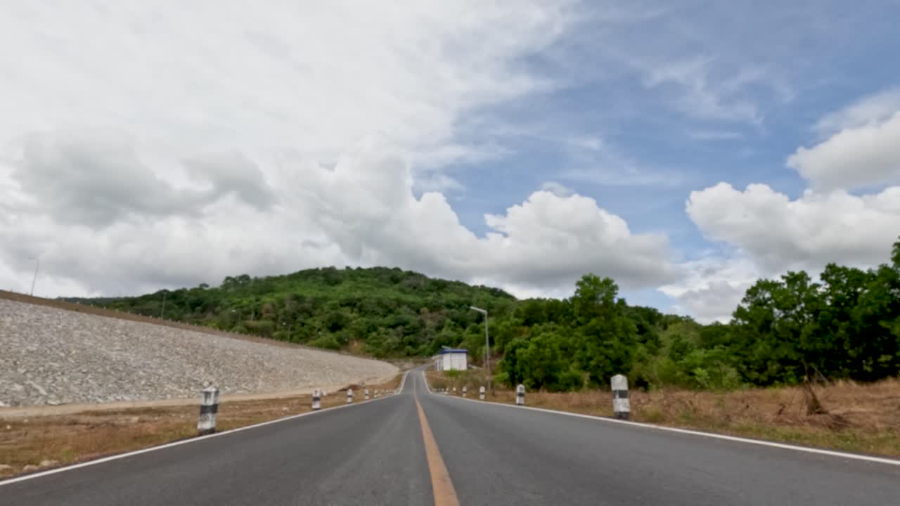 Forward-moving car view on empty rural road, daylight, lush hills, partly cloudy sky, smooth motion