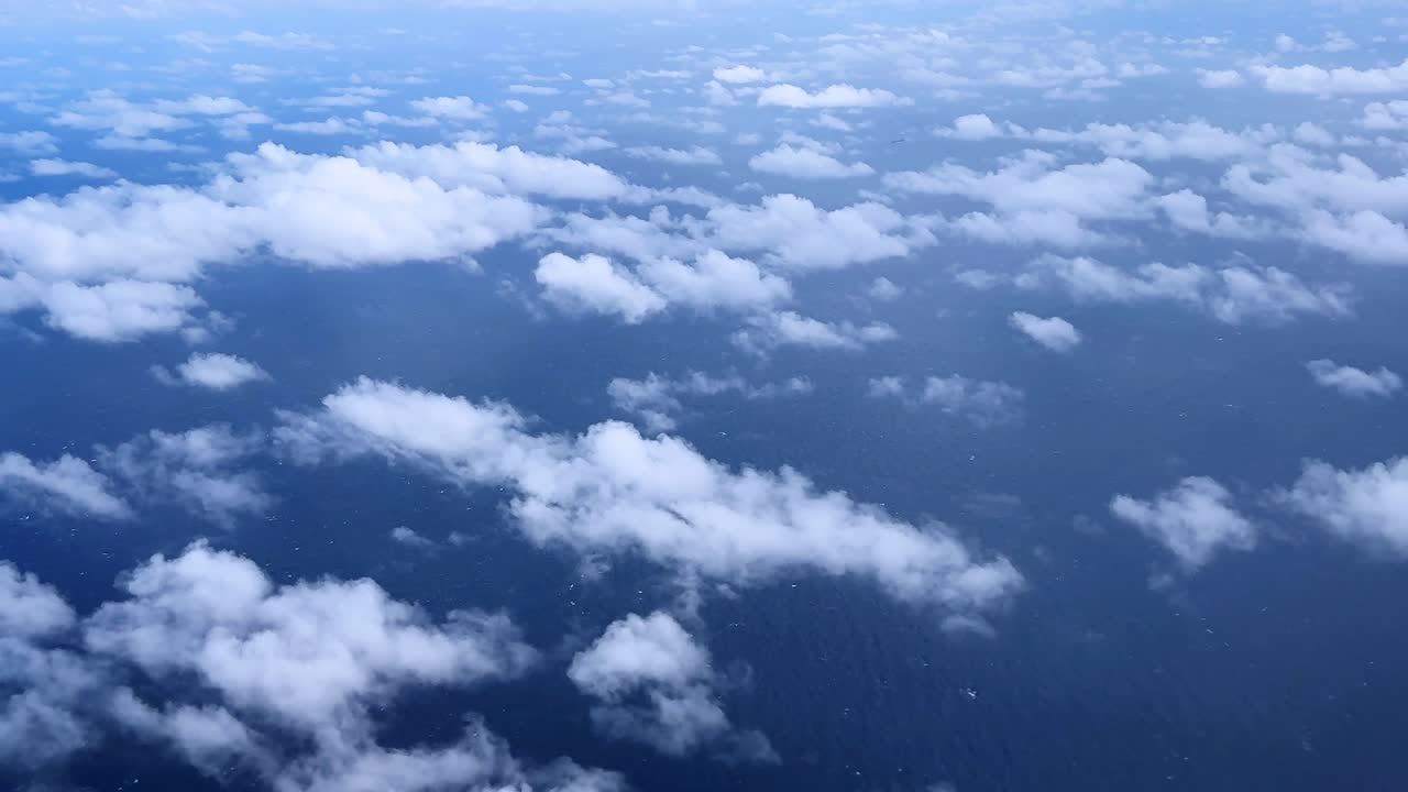 Fluffy white clouds hover over a deep blue sky view from above