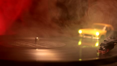 slider shot. disco de vinilo vintage tocando en el reproductor y la guitarra acústica en el fondo con humo de naranja de fuego. concepto de crimen o blues con instalación de automóvil de juguete. enfoque selectivo