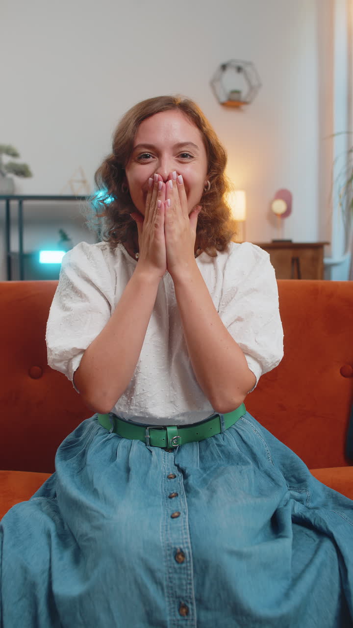 Happy young woman watching tv celebrating success winning lottery luck victory sitting on sofa