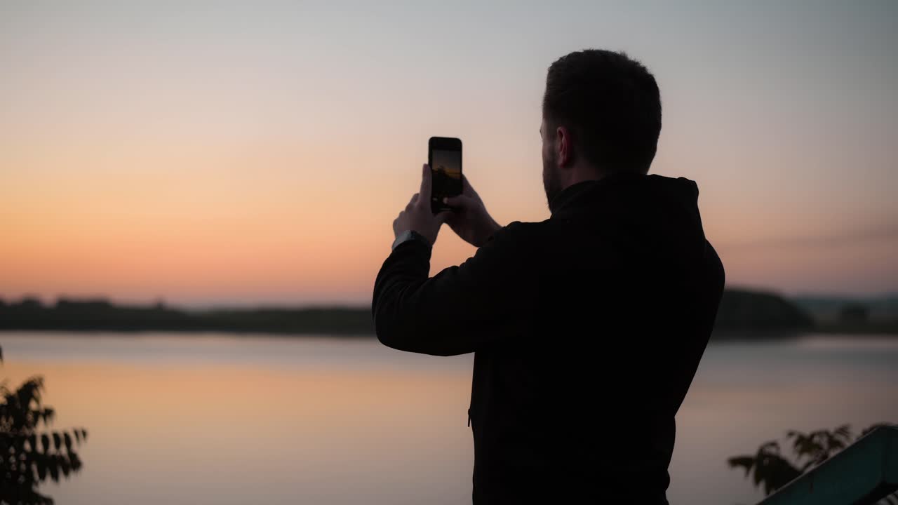 Medium shot of a man taking photos of a panoramic view with his smartphone before the sunrise