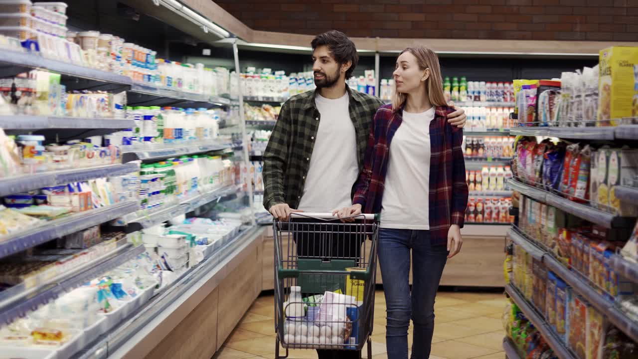 커플 이 슈퍼마켓 에서 카트 를 타고 쇼핑 하고 있다