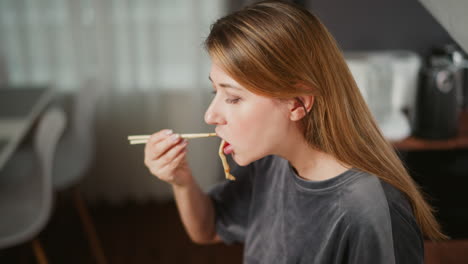 hungry girl enjoys breakfast using chopsticks, sitting in bright modern kitchen with soft natural light and blurred dining chair in background