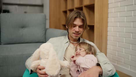 father and daughter play together with soft toy, sitting on the chair