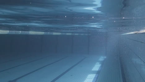 underwater shot of a young female with cap and goggles jumping into the pool