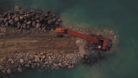 construction of a new breakwater at sea by excavator machine, top down to pullback reveal view