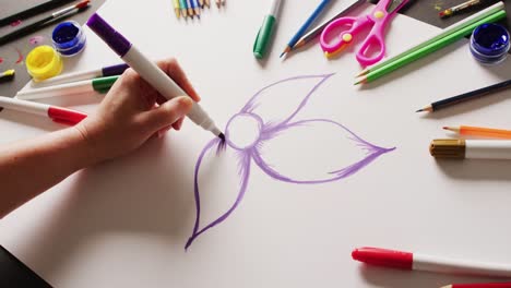 Vídeo-De-Una-Flor-Dibujada-A-Mano-Con-Un-Bolígrafo-Morado-Sobre-Papel,-Con-Materiales-De-Arte-Dispuestos-Sobre-La-Mesa