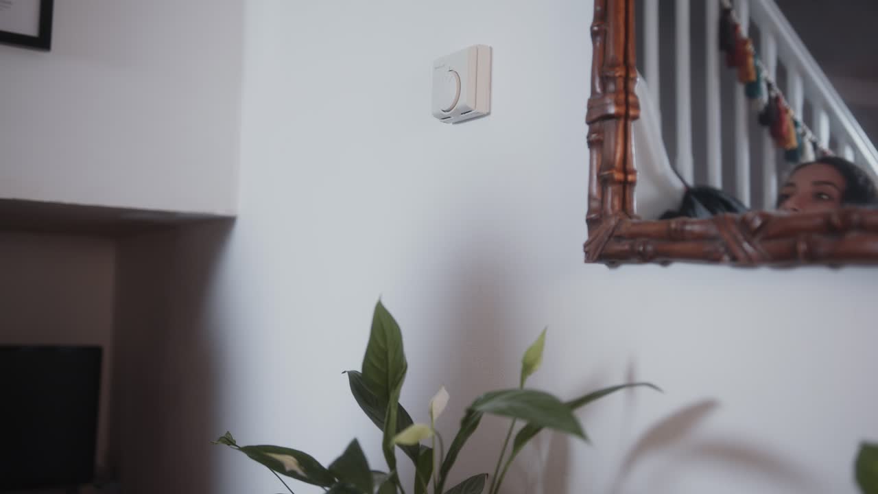 Woman adjusting the dial on thermostat, lowering the temperature to save on energy bills during the cost of living crisis