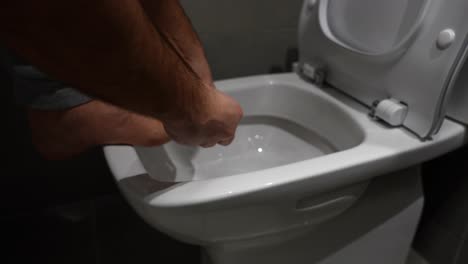 man trimming toenails with clipper over toilet in modern bathroom