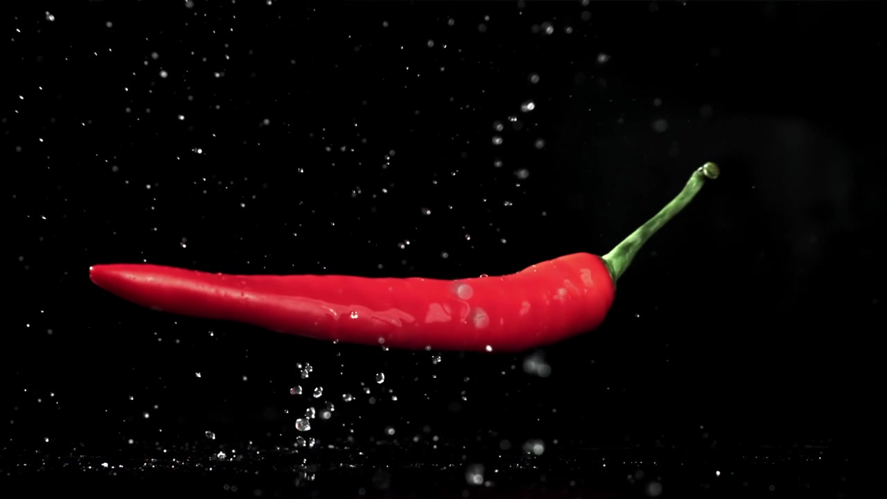 Fresh red chili pepper drops and splashes in water on black background