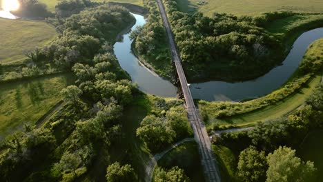 aerial | beautiful river surrounded by greenery with railroad bridge connecting both sides of land