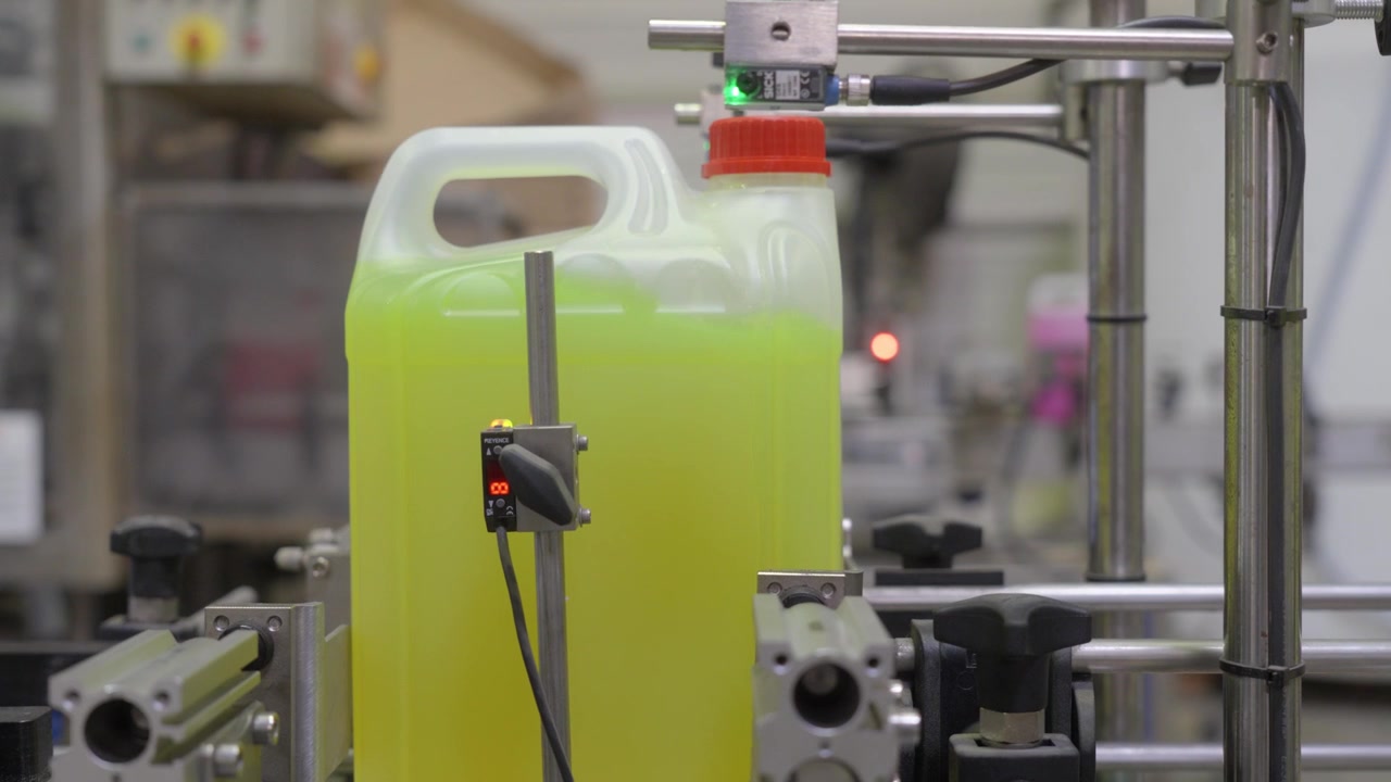 Yellow liquid canisters with red caps moving past sensors and pneumatic valves on production line