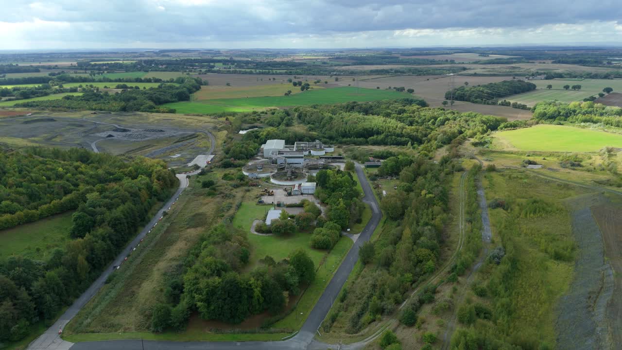 Aerial drone cinematic panorama of sewage treatment facility with clarifying tanks and rural landscape of Yorkshire England featuring green hills and farmland