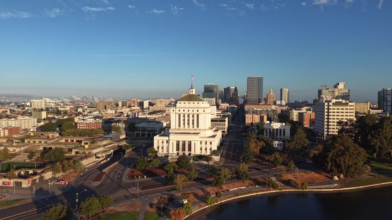 Video aereo con drone sopra il Lago Merritt a Oakland, California, all'alba, che mostra lo skyline della città, il tribunale della Contea di Alameda, l'acqua tranquilla e la luce nitida del mattino con un vivido contrasto di colori