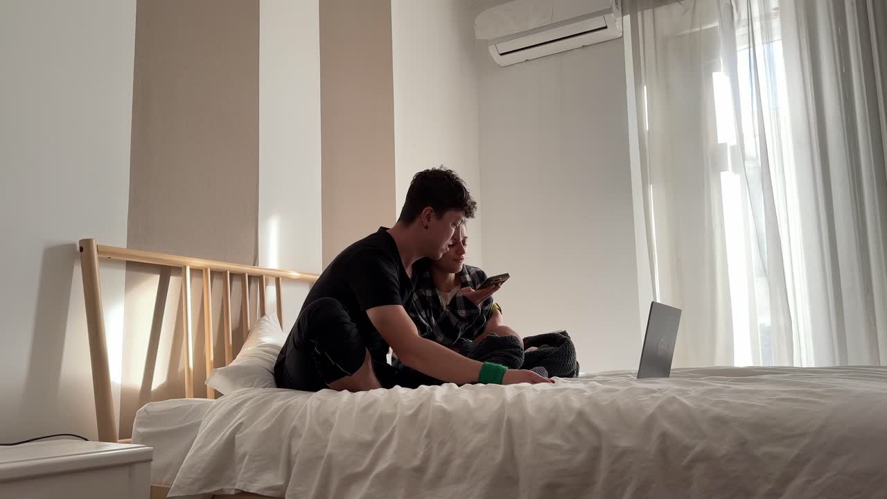 Couple relaxing on a bed looking at laptop and phones
