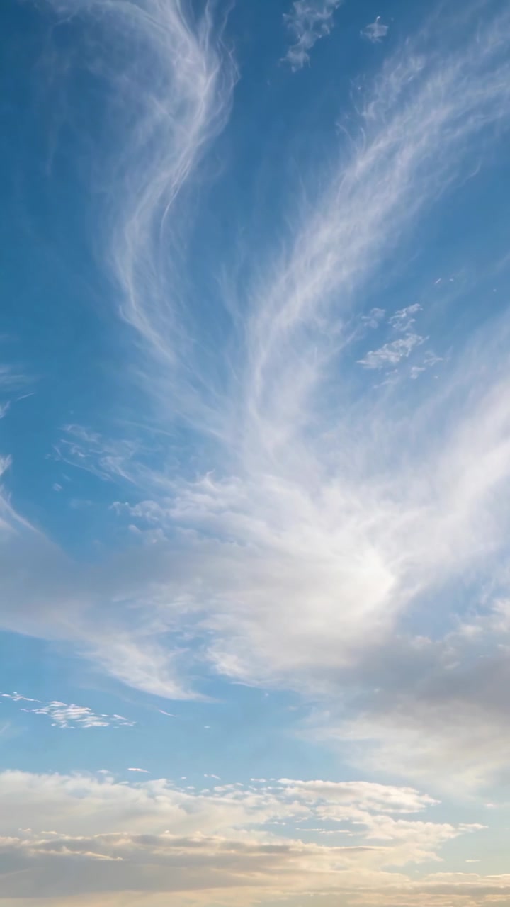 Vertikal video: Kraftig vind skubber tynde cirrusskyer, der driver hen over blå himmel med lavere skyer