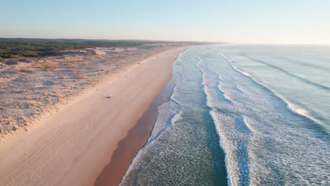 drone following the coastline along a sandy beach with rolling ocean waves