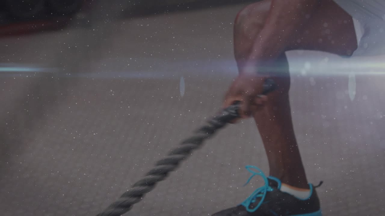 Male athlete gripping ropes, dropping into squat, swinging blur waves with lens flare for training