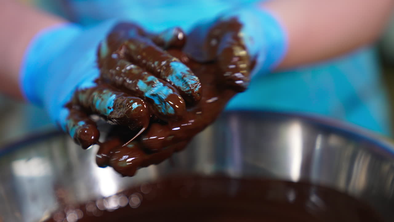 Gloved confectioner's hands covered with chocolate take white creamy balls for coating. Handmade truffle manufacturing. Close up.