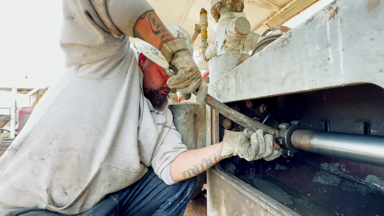 Big Caucasian bearded man in protective helmet using a wrench on the metal pipe. Portrait of a person working in gas production industry.
