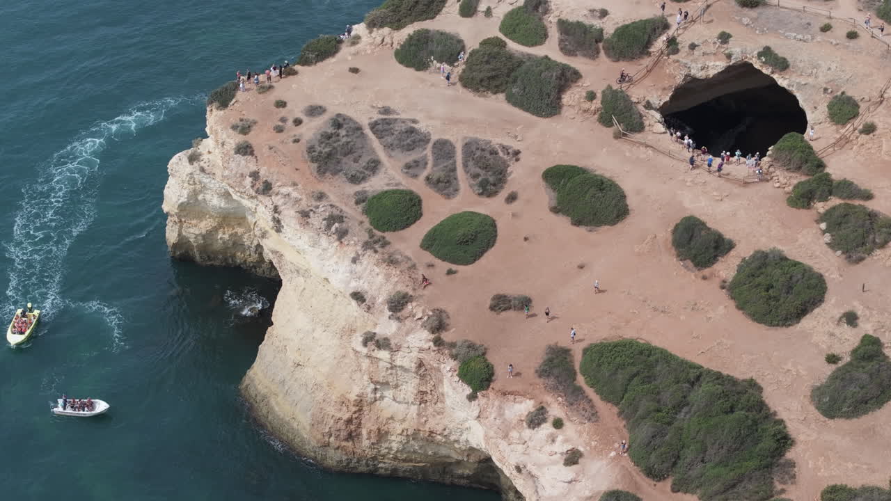 Aerial drone view of the Benagil Sea Cave and Atlantic Ocean coastline in Benagil, Algarve, Portugal, Europe. Boats and people sightseeing. Tourism concept