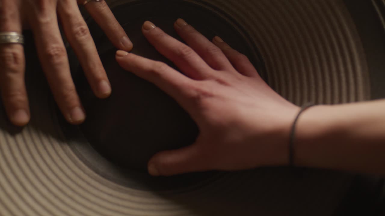 Top-down view of two people's hands resting on a large speaker driver, feeling the physical vibrations of deep bass music