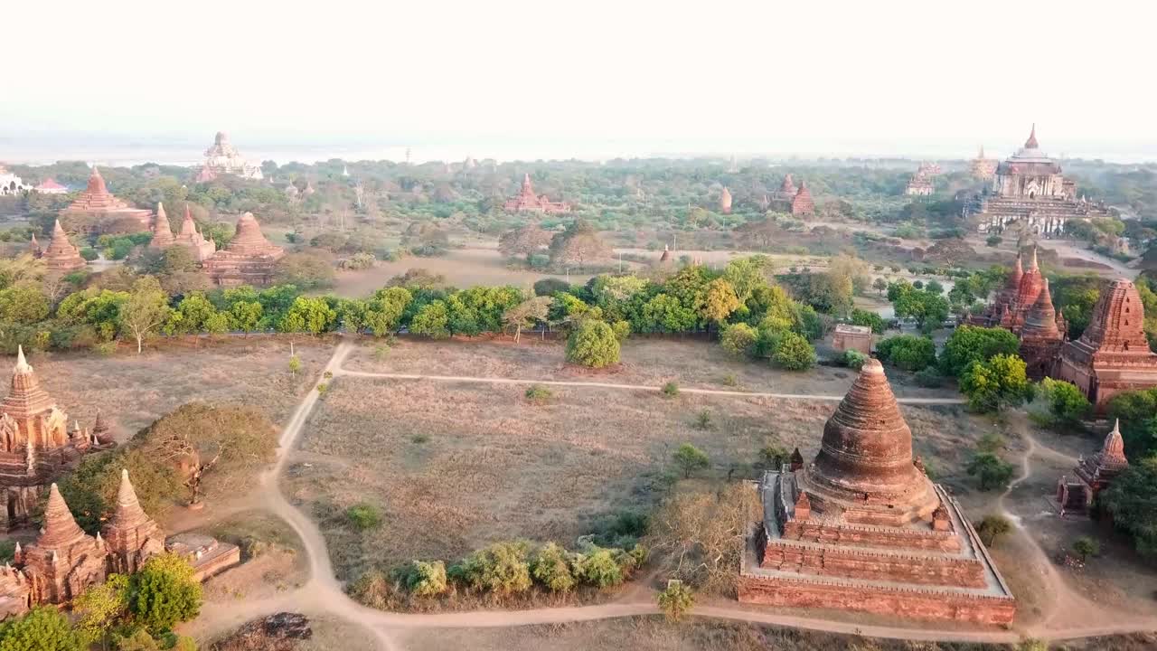 Stunning aerial view capturing the Bagan archaeological zone at sunrise, revealing numerous buddhist temples, pagodas, and stupas across the serene landscape, drone reveal