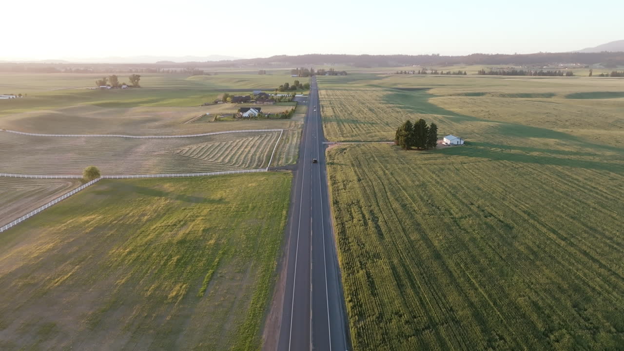 Drone view of a long country road running through patchworked farmland near Spokane at golden hour