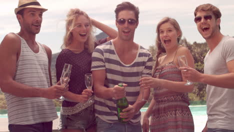 happy friends opening champagne bottle by the pool
