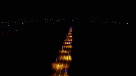 Aerial-night-view-of-a-lit-highway-stretching-into-city-lights,-cars-in-motion,-urban-vibe