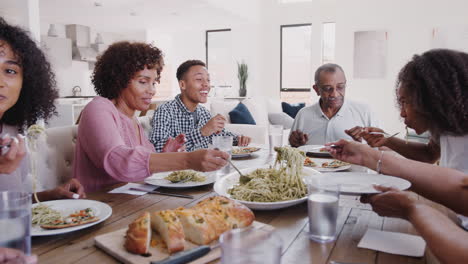 Three-generation-black-family-sitting-at-dinner-table-serving-spaghetti,-panning-shot