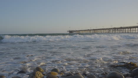 panning shot of the end of ventura pier panning into the pacific ocean with huge waves crashing into the shores of ventura beach at sunset located in southern california