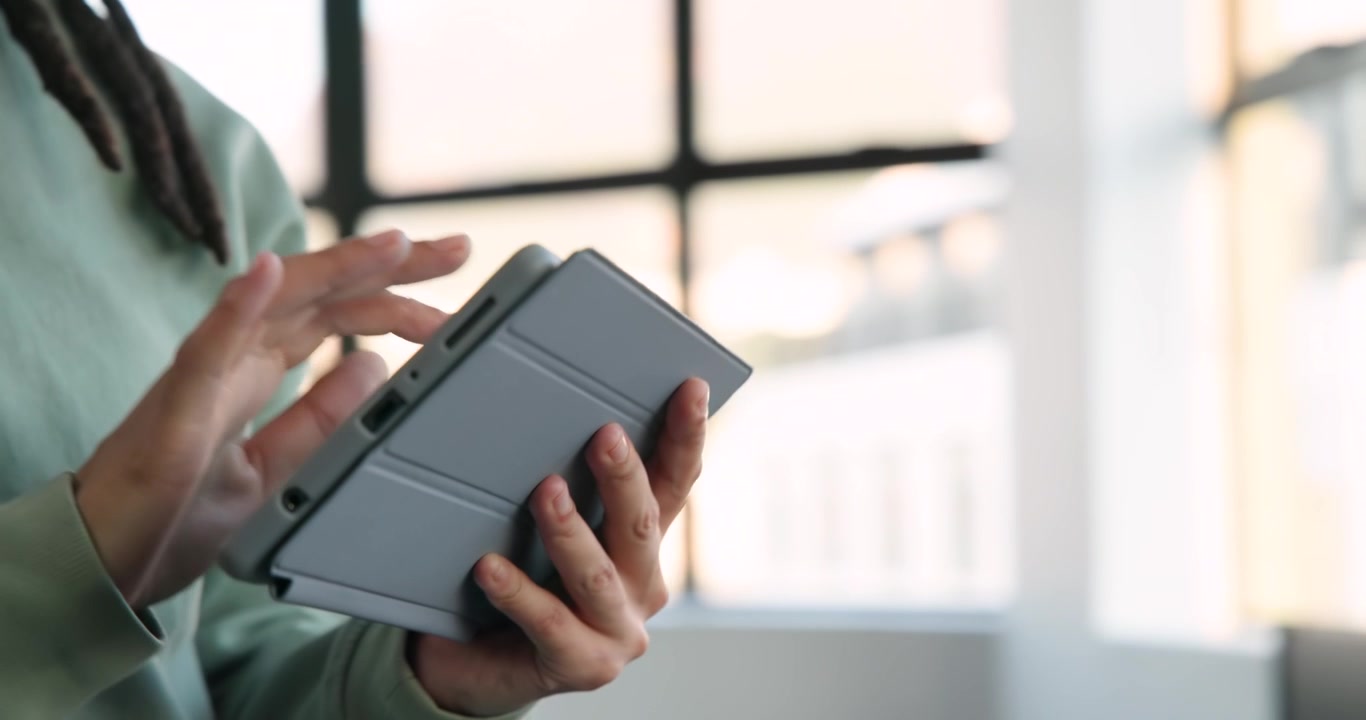 African non-binary person holding tablet, right hand tapping folio ports, navigating app in office
