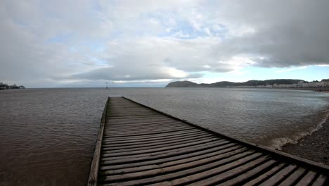 time lapse waves pulse under empty wooden jetty boardwalk leading to overcast ocean seascape