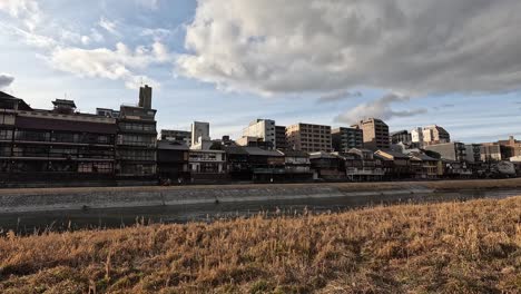 traditional wooden houses along the kamo river in kyoto framed by golden grass and dramatic afternoon clouds