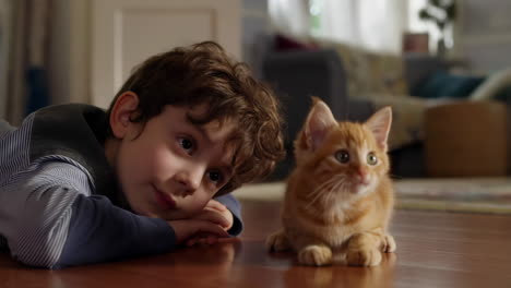 a young boy and an orange tabby kitten on a wooden floor
