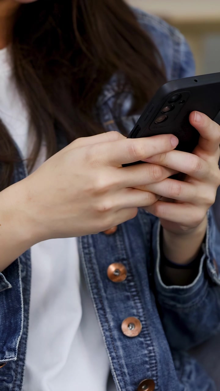 Primo piano di una donna asiatica con una giacca di jeans che digita sul suo smartphone