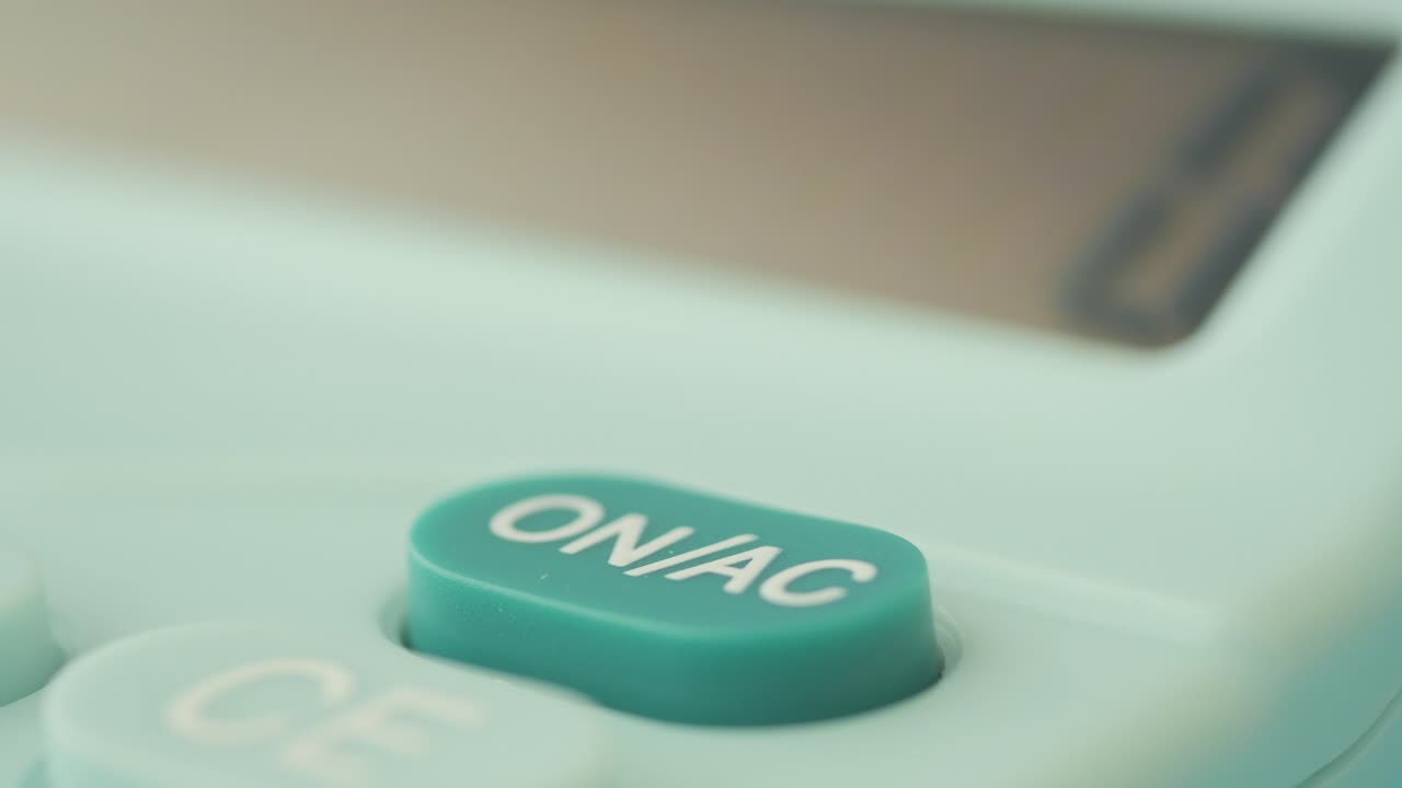 Finger Pressing On/Off Button of a Light Teal Calculator