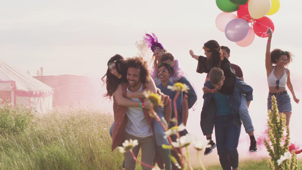 grupo de jóvenes amigos emocionados caminando por el sitio del festival de música llevando bengalas y globos