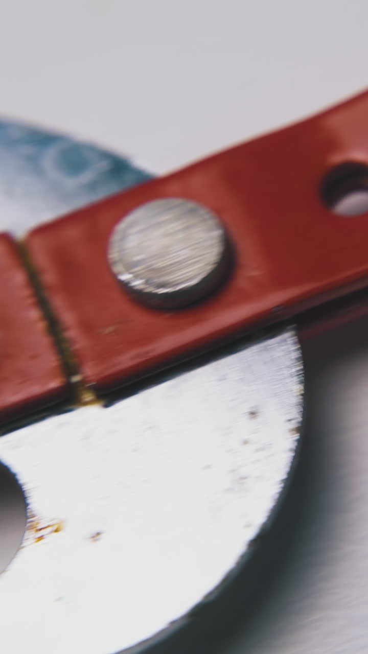 motion past old fashioned sharp metal can opener with red handle lying on clean white surface macro