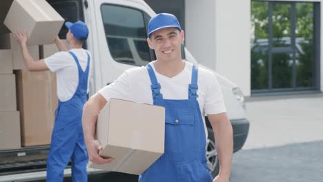 dos jóvenes trabajadores de una compañía de mudanzas están cargando cajas y muebles en un minibus