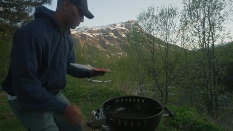 man using a tong to move large steak from plate to grill while outdoors