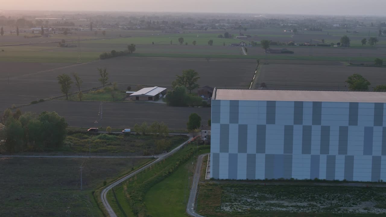 NewCold automatiseret kølelager nær motorvejsafkørsel A1 i Fiorenzuola d’Arda, Piacenza, Emilia Romagna, Italien, med høj struktur og stort fodaftryk i det landbrugsprægede Po-dal-landskab ved solnedgang
