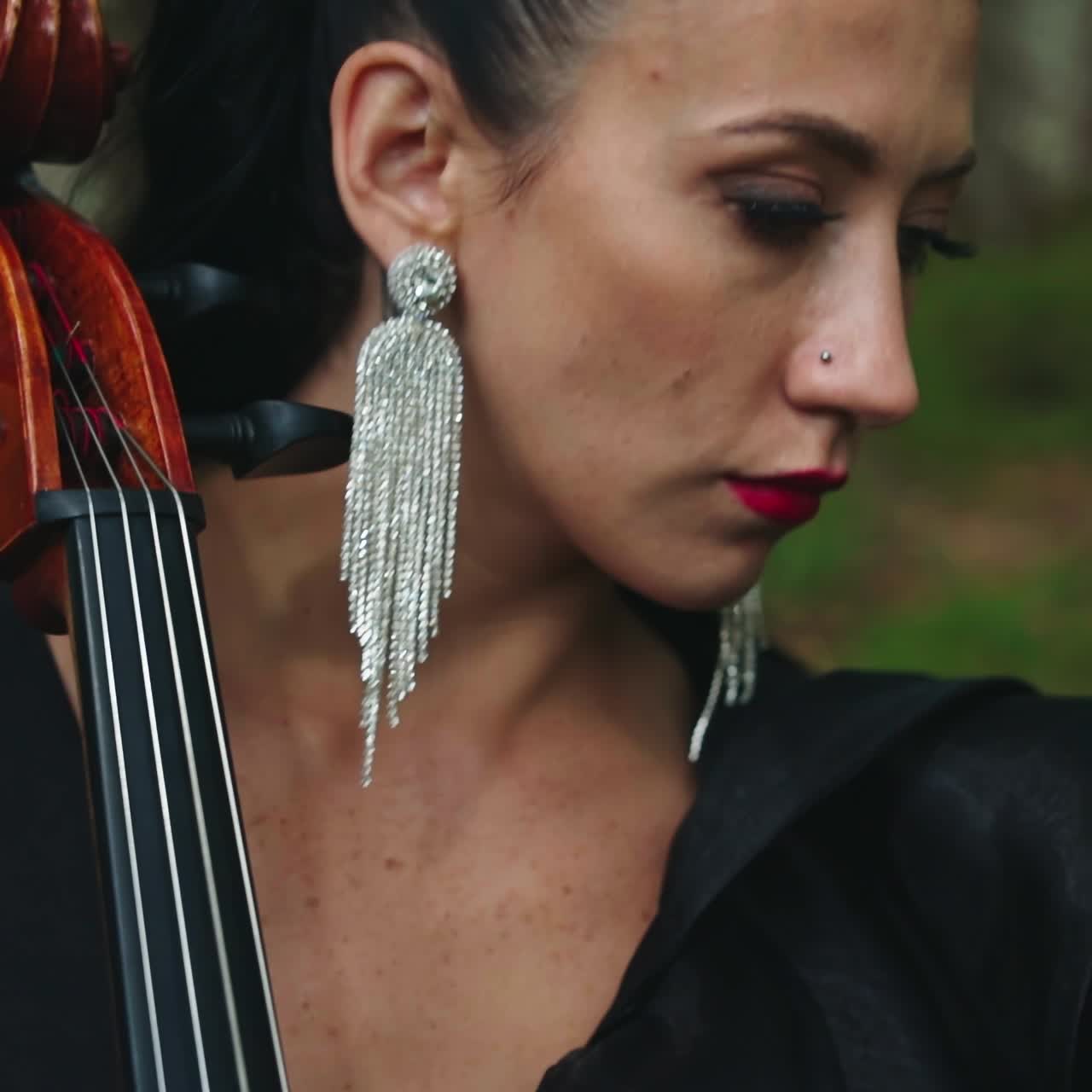 Female musician performs music outdoors. Portrait of a woman with luxury earrings playing the musical instrument. Close-up.